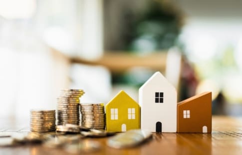 Stacks of coins next to wooden houses represent a fall in mortgage rates